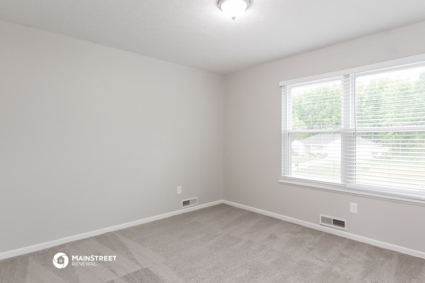 the spacious living room with two windows and carpeting