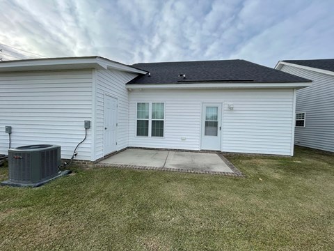 A white house with a grey air conditioner in front.