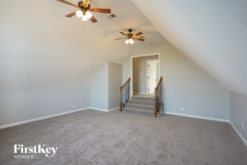 a carpeted loft with a ceiling fan and a staircase