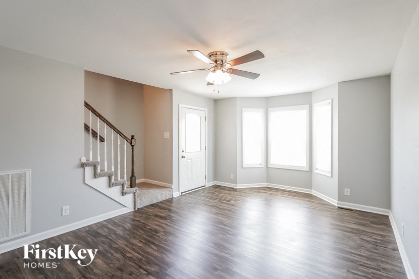 an empty living room with a ceiling fan and a staircase
