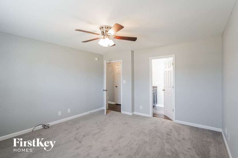 an empty living room with a ceiling fan and a door to a bathroom
