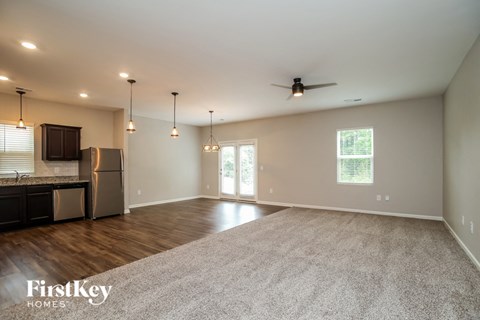 an empty living room with a kitchen and a ceiling fan