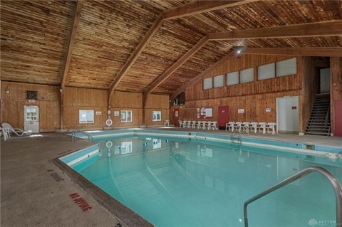 A large indoor swimming pool with a wooden ceiling and deck chairs.