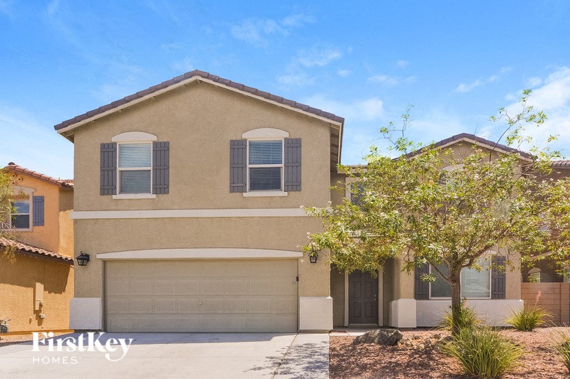A beige house with a garage door and a tree in front.