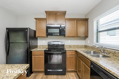 A kitchen with a black refrigerator, black stove, and wooden cabinets.