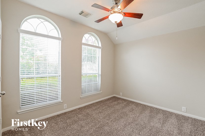 an empty living room with two windows and a ceiling fan