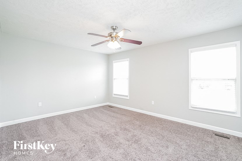 an empty room with a ceiling fan and two windows