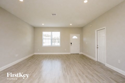 A spacious empty room with wooden flooring and a window.