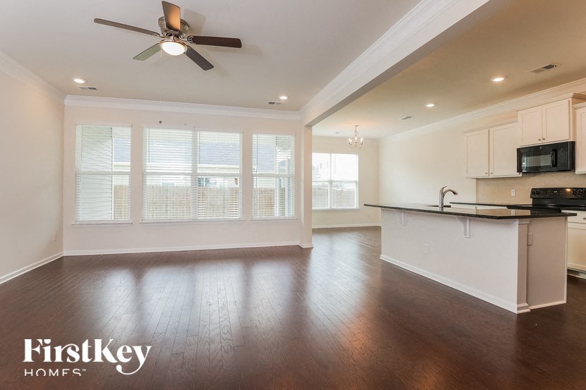 an empty living room with a kitchen and a ceiling fan