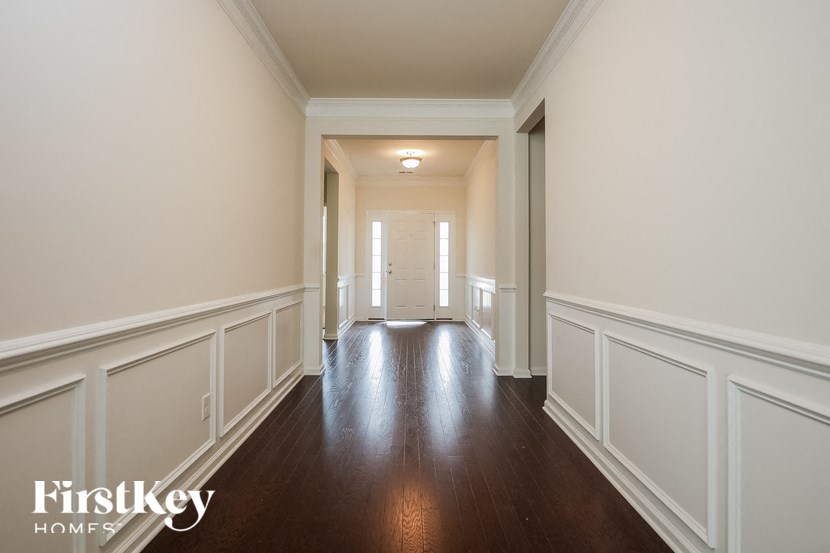 a hallway with white walls and wood flooring and a door to a house