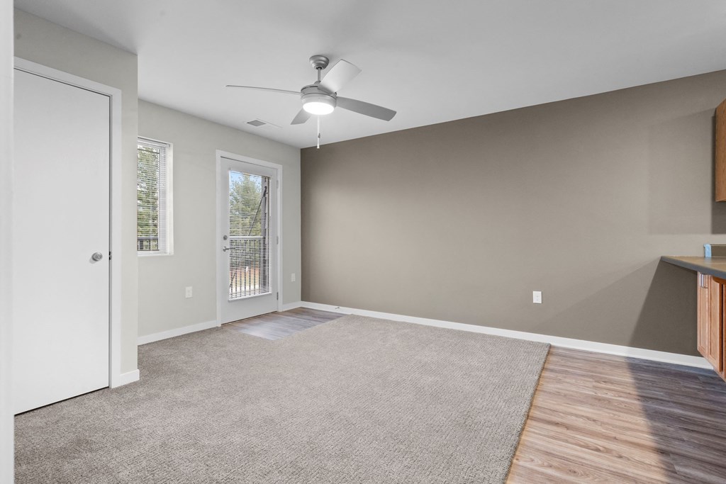 an empty living room with a ceiling fan and a door to a balcony