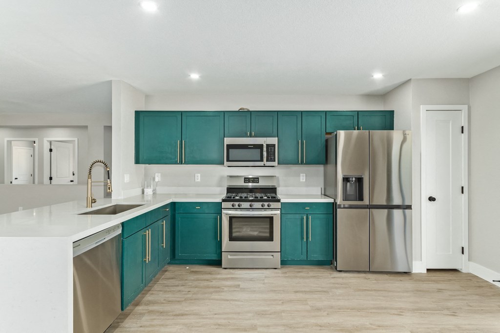 A modern kitchen with teal cabinets and stainless steel appliances.