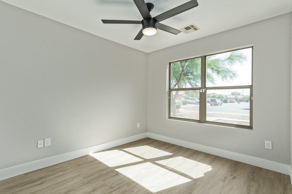 A room with a ceiling fan and a window overlooking a parking lot.
