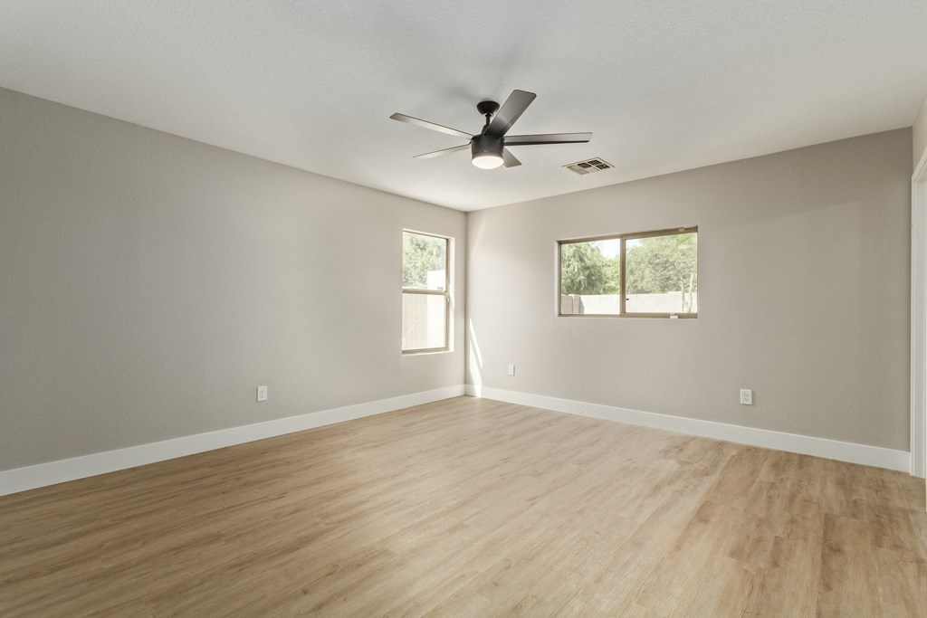A room with a ceiling fan and two windows.