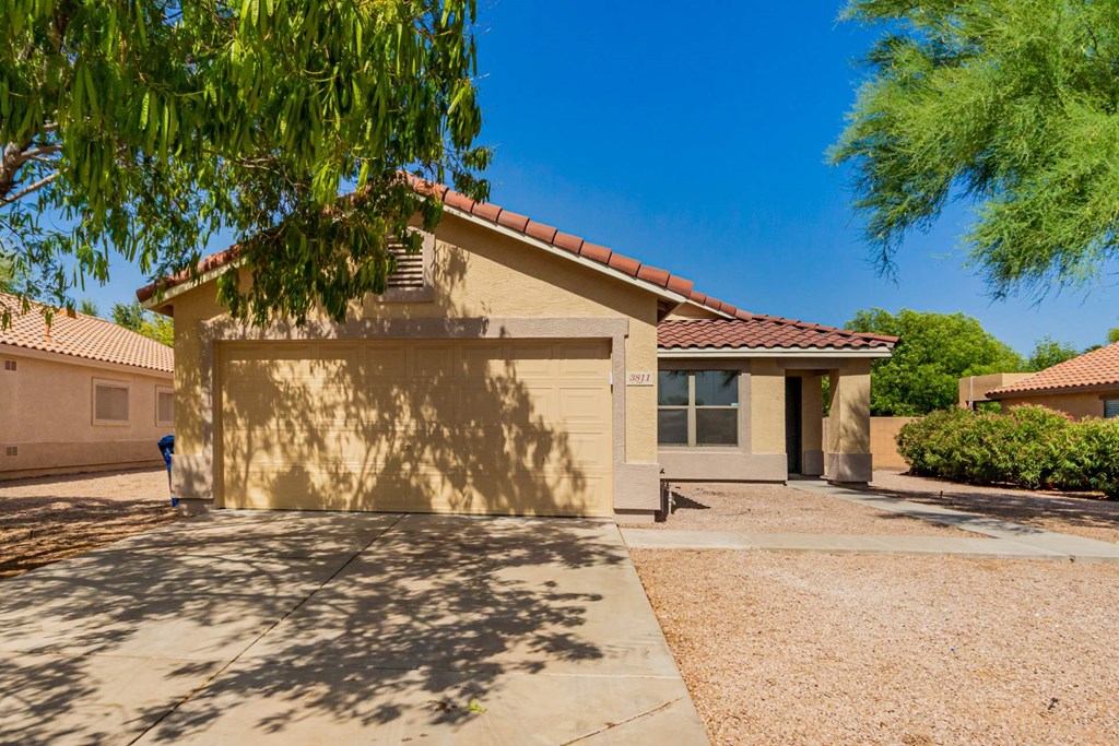 A house with a brown roof and tan walls with a driveway in front.
