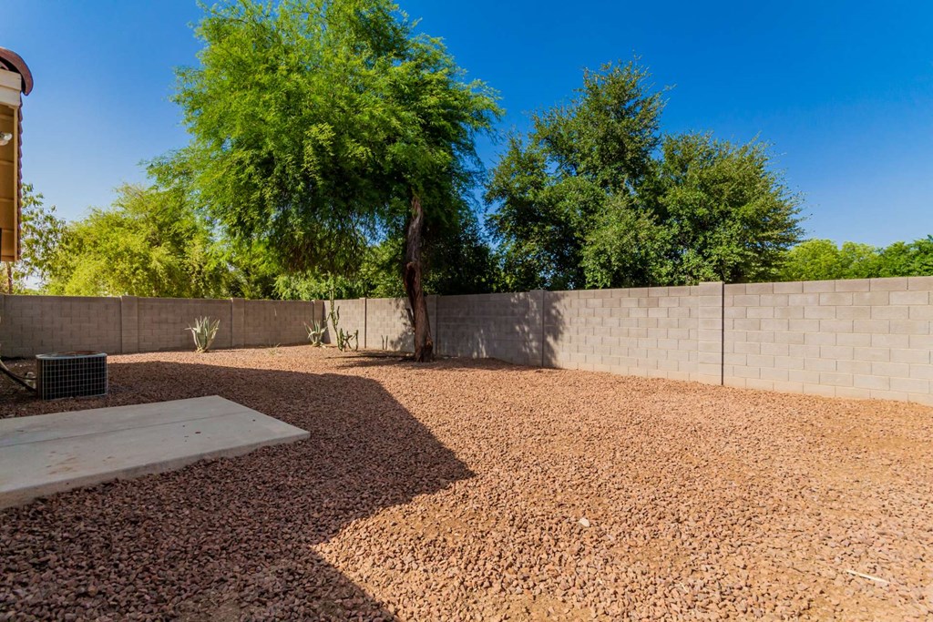 A backyard with a gravel ground and a concrete wall.