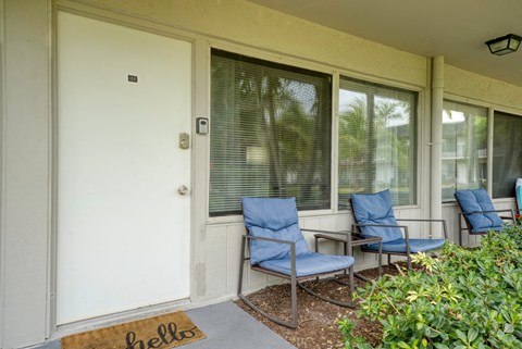 the front porch of a house with blue chairs and a white door