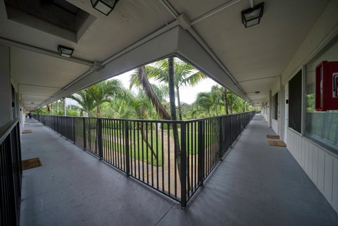 the covered walkway of an apartment building with a view of the grass and trees
