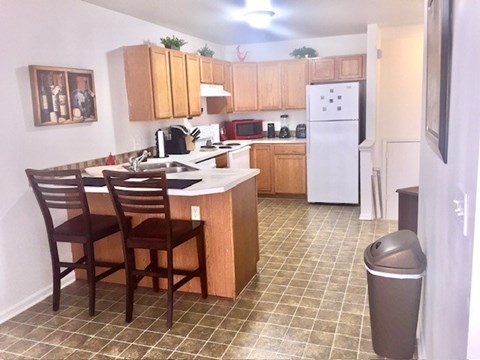 A kitchen with a white refrigerator and brown chairs.