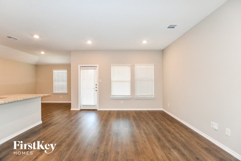 an empty living room with wood flooring and a kitchen