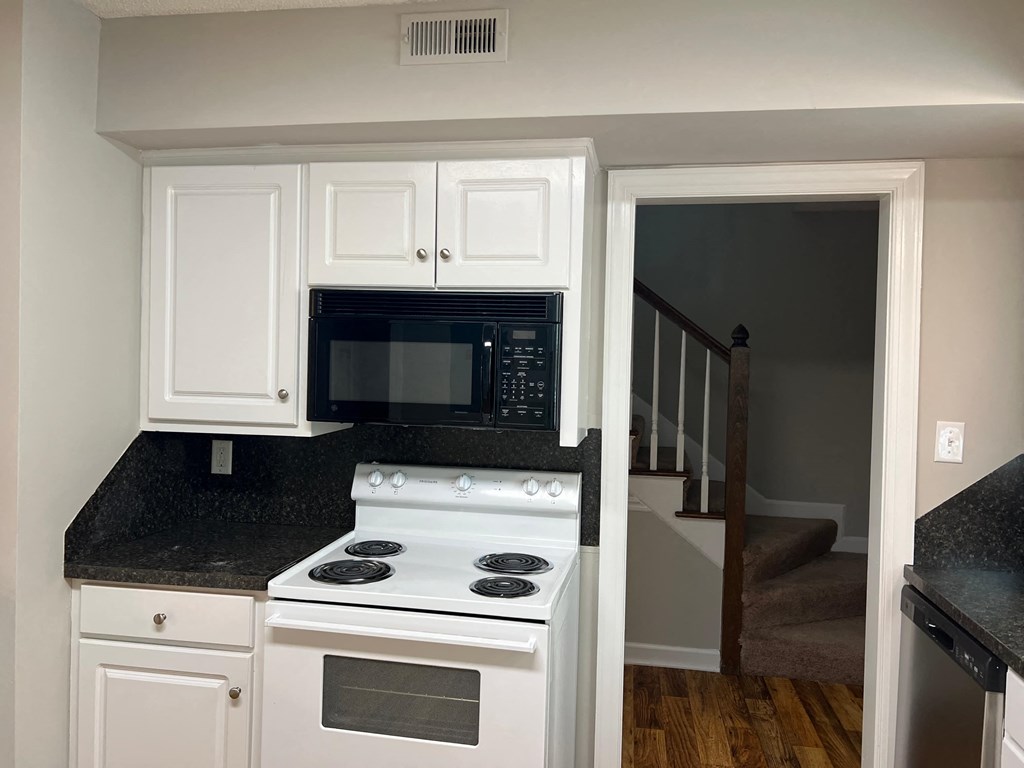 A white kitchen with a black microwave and stove.