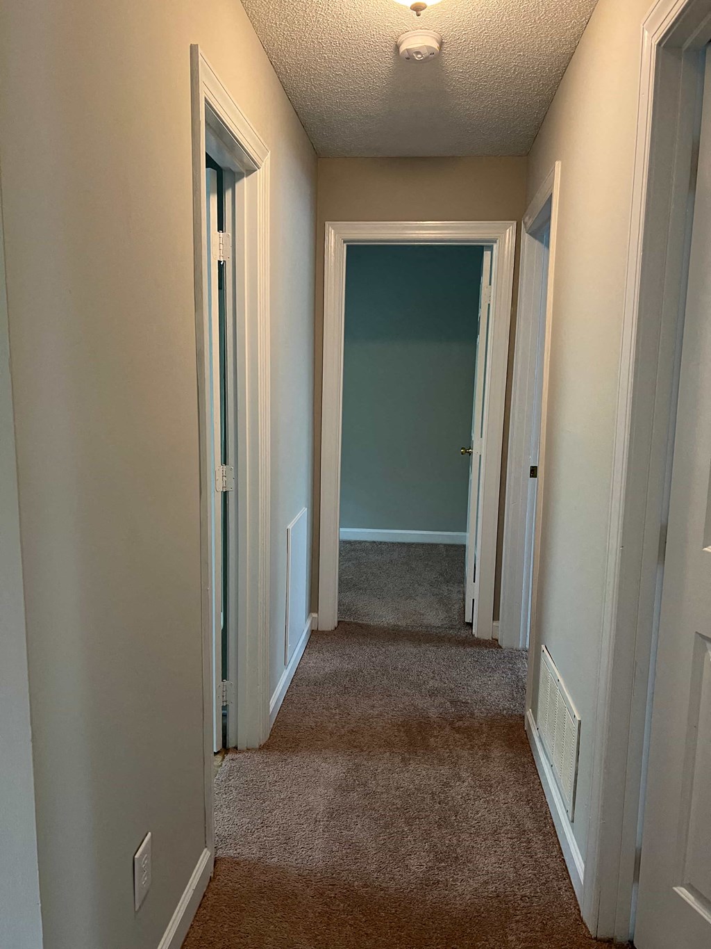 A hallway with white walls and a brown carpet.