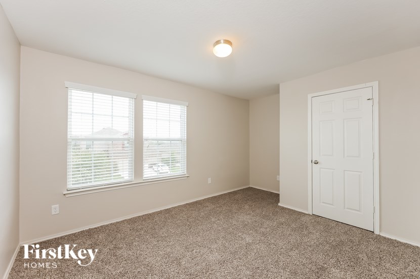 A room with a carpeted floor, a door, and a window with blinds.
