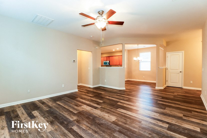 an empty living room with a ceiling fan and a kitchen