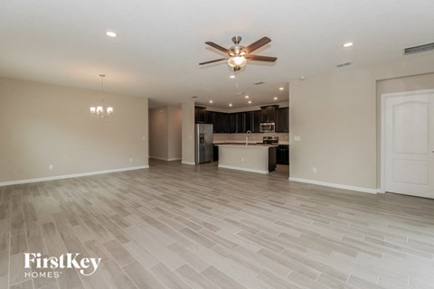 A spacious room with a fan and a kitchen in the background.
