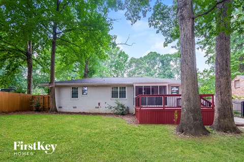 a small white house with a red deck and trees
