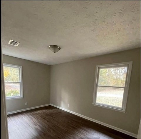 an empty room with a hard wood floor and two windows