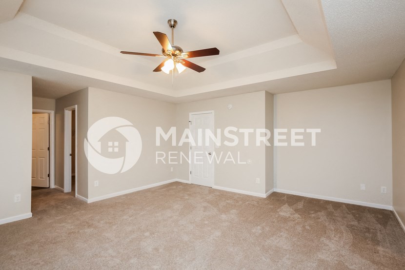 a living room with beige carpet and a ceiling fan