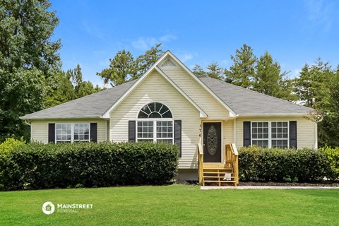 a small yellow house with a lawn and hedges