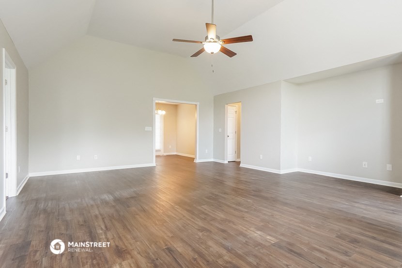 the spacious living room with hardwood flooring and a ceiling fan