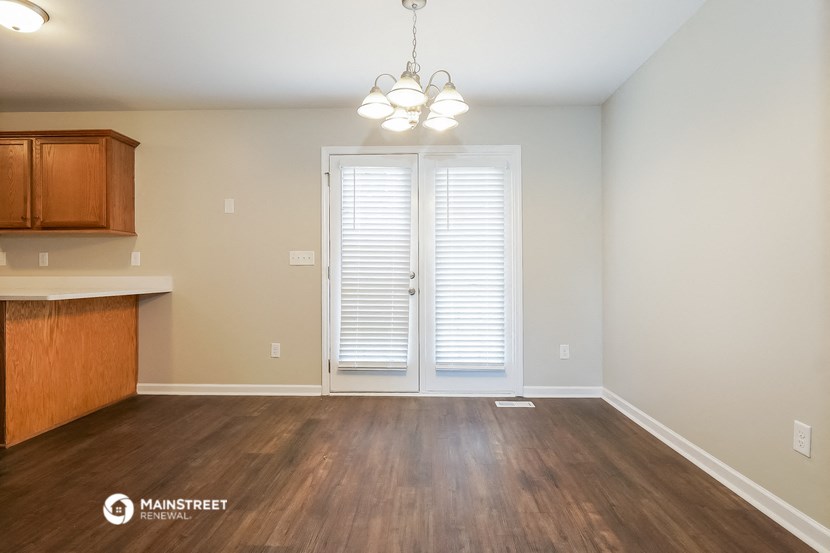 an empty living room with wood flooring and a door to the kitchen