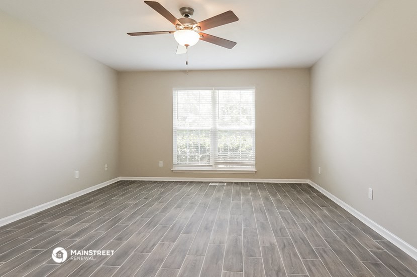 the spacious living room with wood floors and a ceiling fan