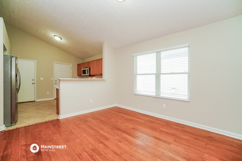 an empty living room with wood floors and a kitchen