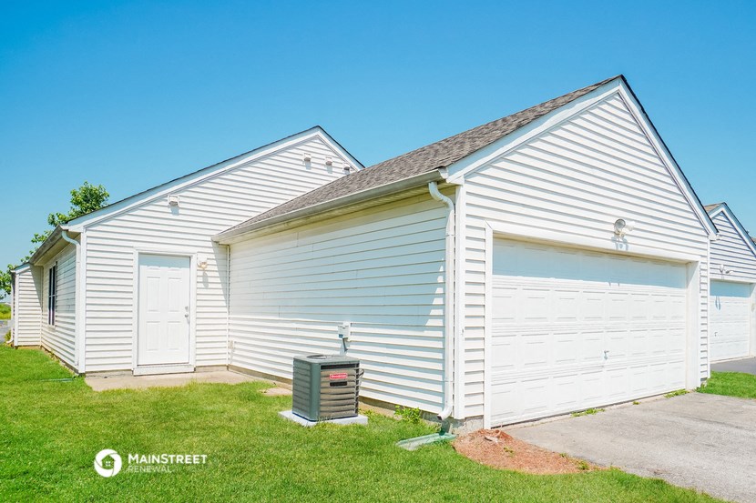 a white building with a garage and a trash can in front of it