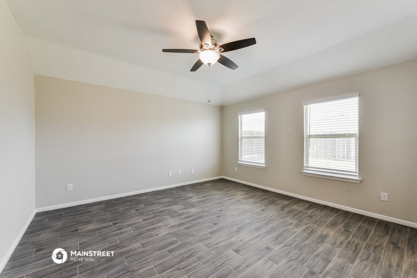 the spacious living room with wood flooring and a ceiling fan