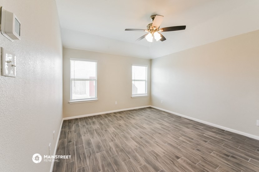 the spacious living room with wood flooring and a ceiling fan