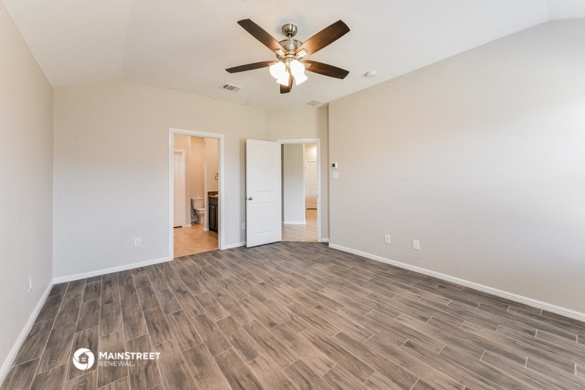 the spacious living room with wood flooring and a ceiling fan