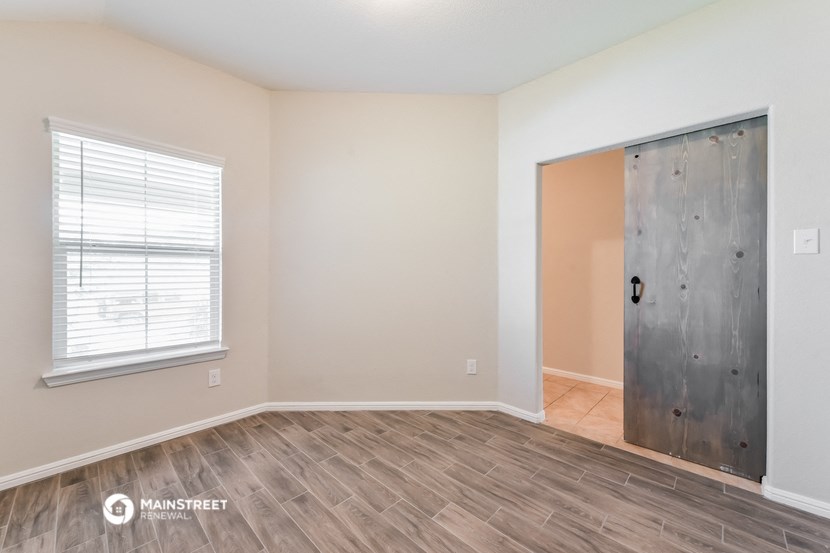 the spacious living room with wood flooring and a door to the bedroom