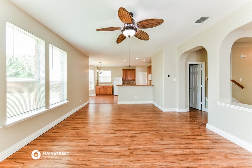an empty living room with a ceiling fan and a kitchen