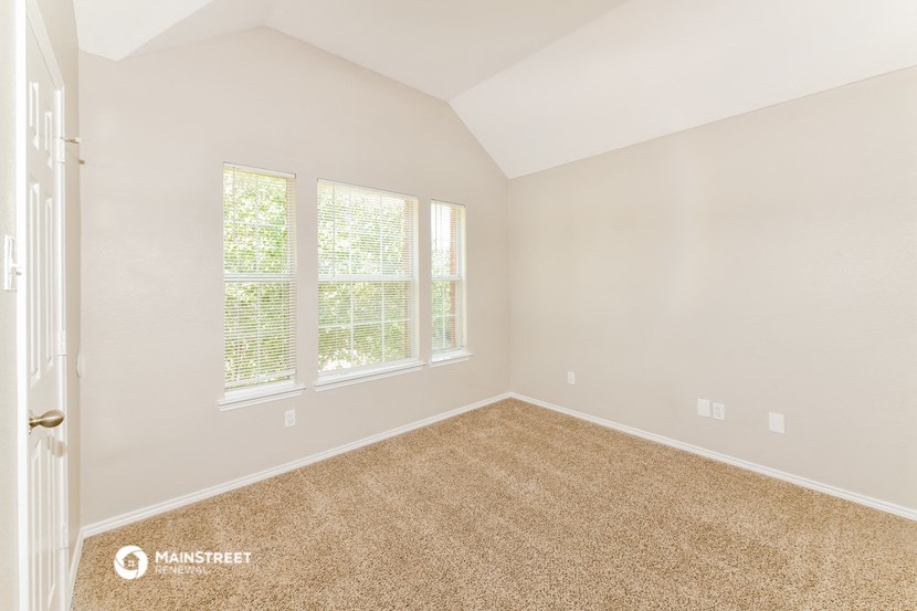 an empty room with carpet and three windows