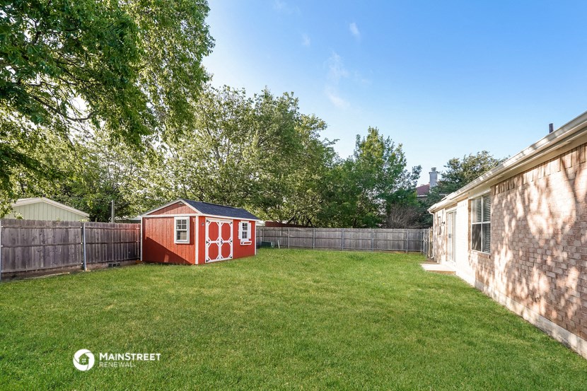a backyard with a red shed and a green lawn and a fence
