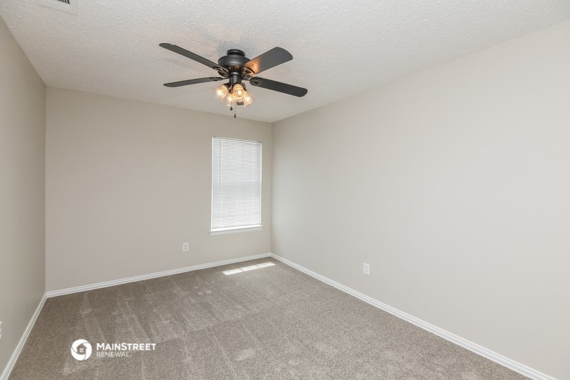 the spacious living room with ceiling fan and carpet