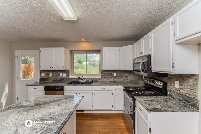 the kitchen has granite counter tops and white cabinets and stainless steel appliances
