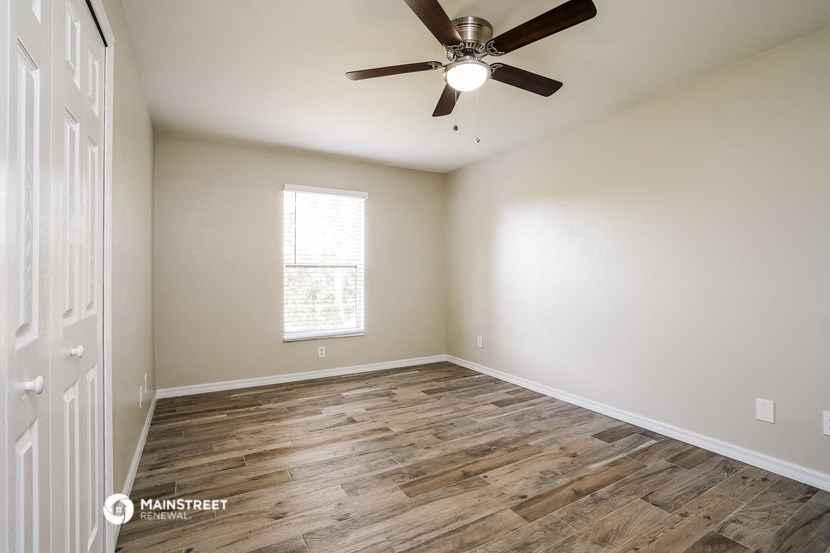 the spacious living room with wood flooring and a ceiling fan