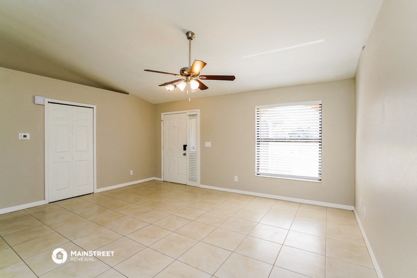 an empty living room with a ceiling fan and tiled floors