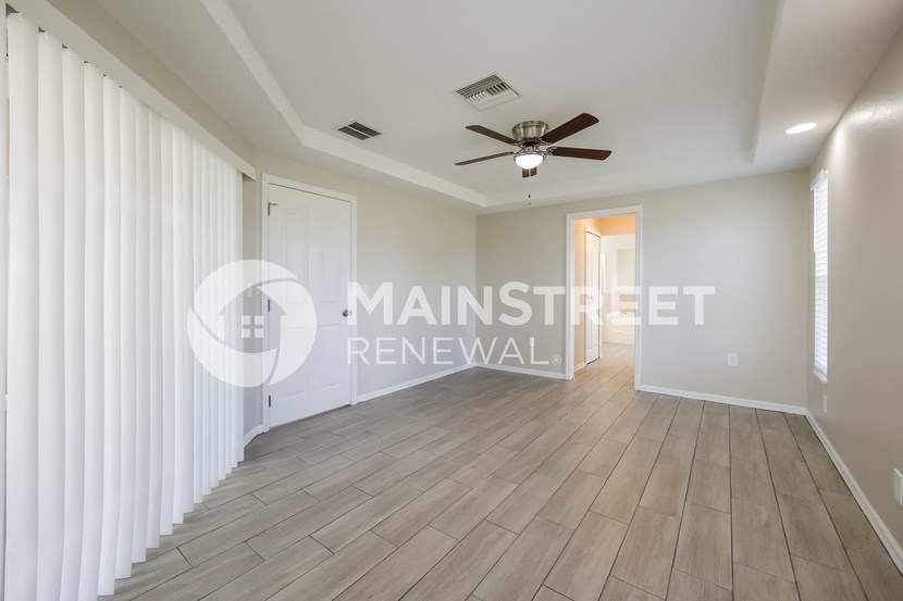 a renovated living room with a ceiling fan and white curtains